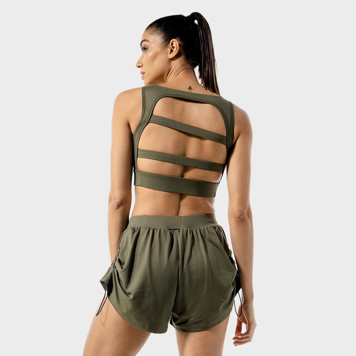 Rear view of a woman wearing an olive-green sports bra with horizontal straps across the open back and matching shorts.
