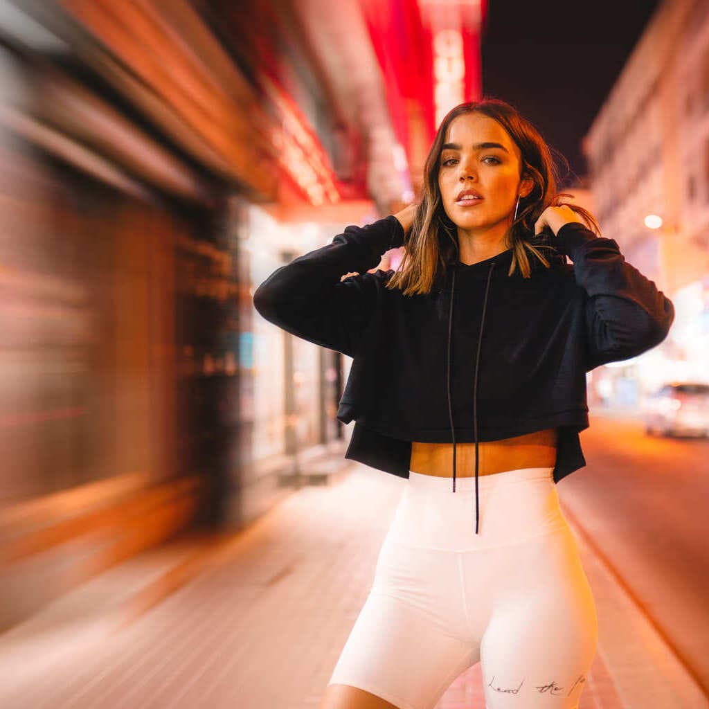 Woman wearing a black cropped hoodie and white cycling shorts on an illuminated street at night.