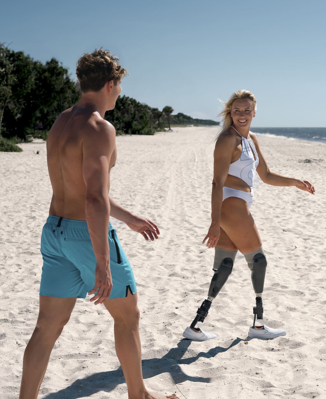 Karlmaður gengur á strönd í túrkísbláum Arena Evo Side Zip Pockets Beach Boxer sundbuxum