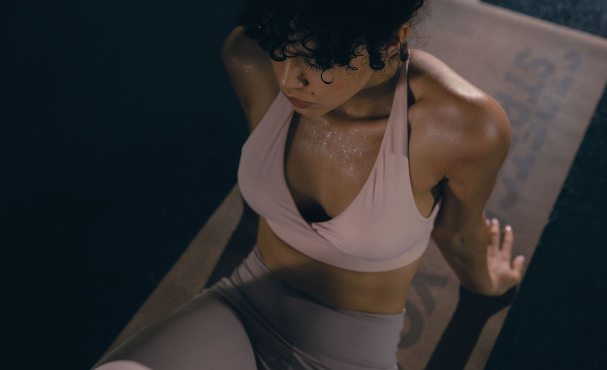 Woman in a pale pink sports bra and leggings exercising on a mat, viewed from above.