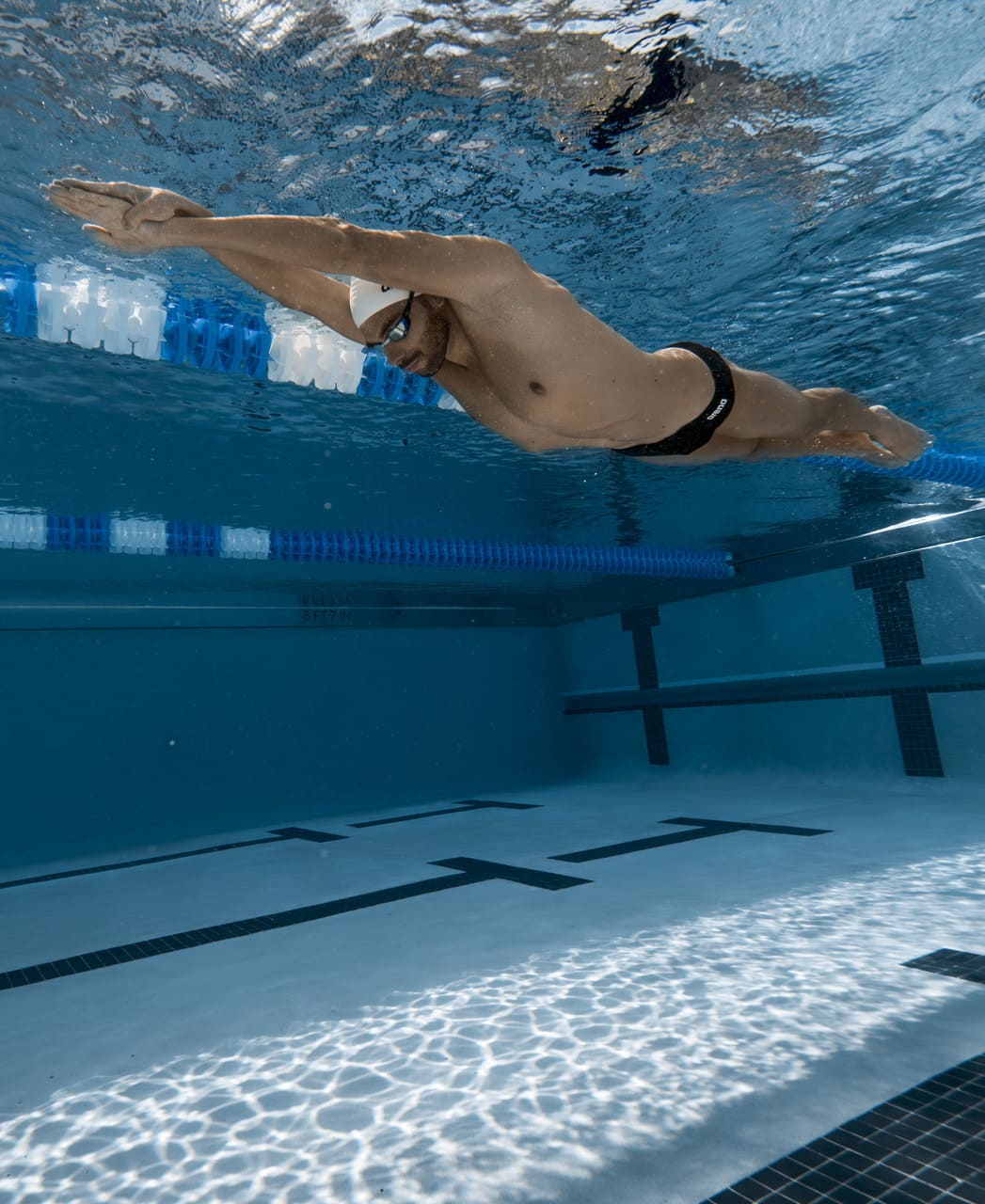 Sundmaður í svartri Arena Team Swim Brief Solid sundskýlu í straumlínulagaðri stöðu undir vatni, stutt snið sem dregur ekki úr hreyfanleika