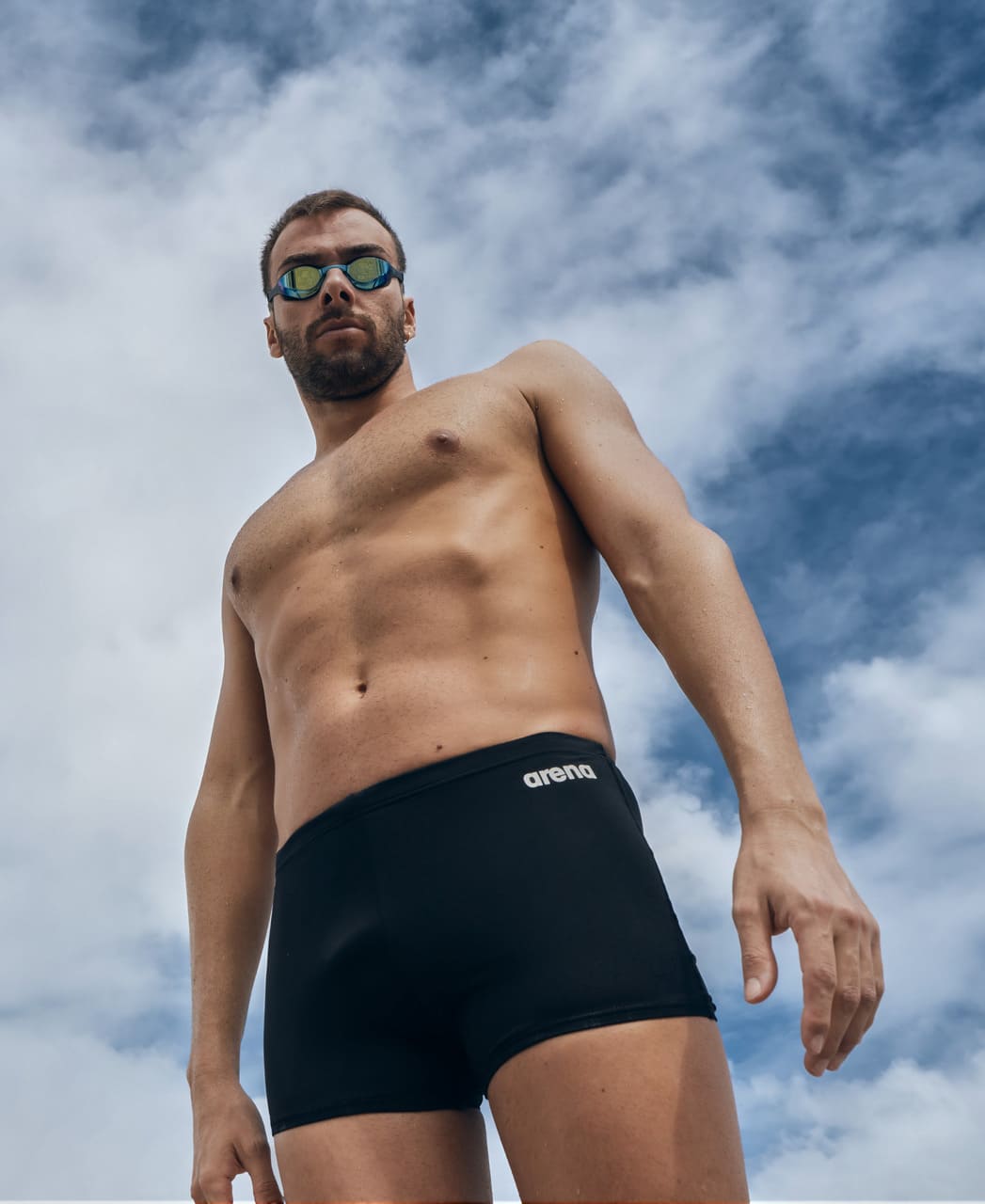 Klórþolin sundskýla fyrir herra í svörtu frá Arena. Team sundskýlan er framleidd úr MaxLife Eco sundfataefni Arena úr 100% pólýester (að hluta endurunnu pólýester) sem gerir þær að góðum kosti fyrir íslenskar sundlaugar með klór. Lífstílsmyndin sýnir karlmann standa í Team sundskýlunni með sundgleraugu