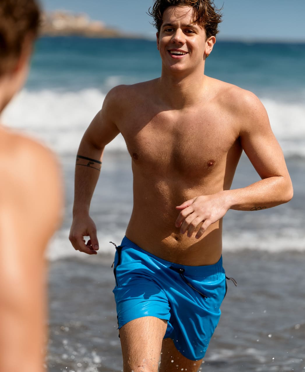 Karlmaður hleypur á strönd í túrkísbláum Arena Evo Side Zip Pockets Beach Boxer sundbuxum