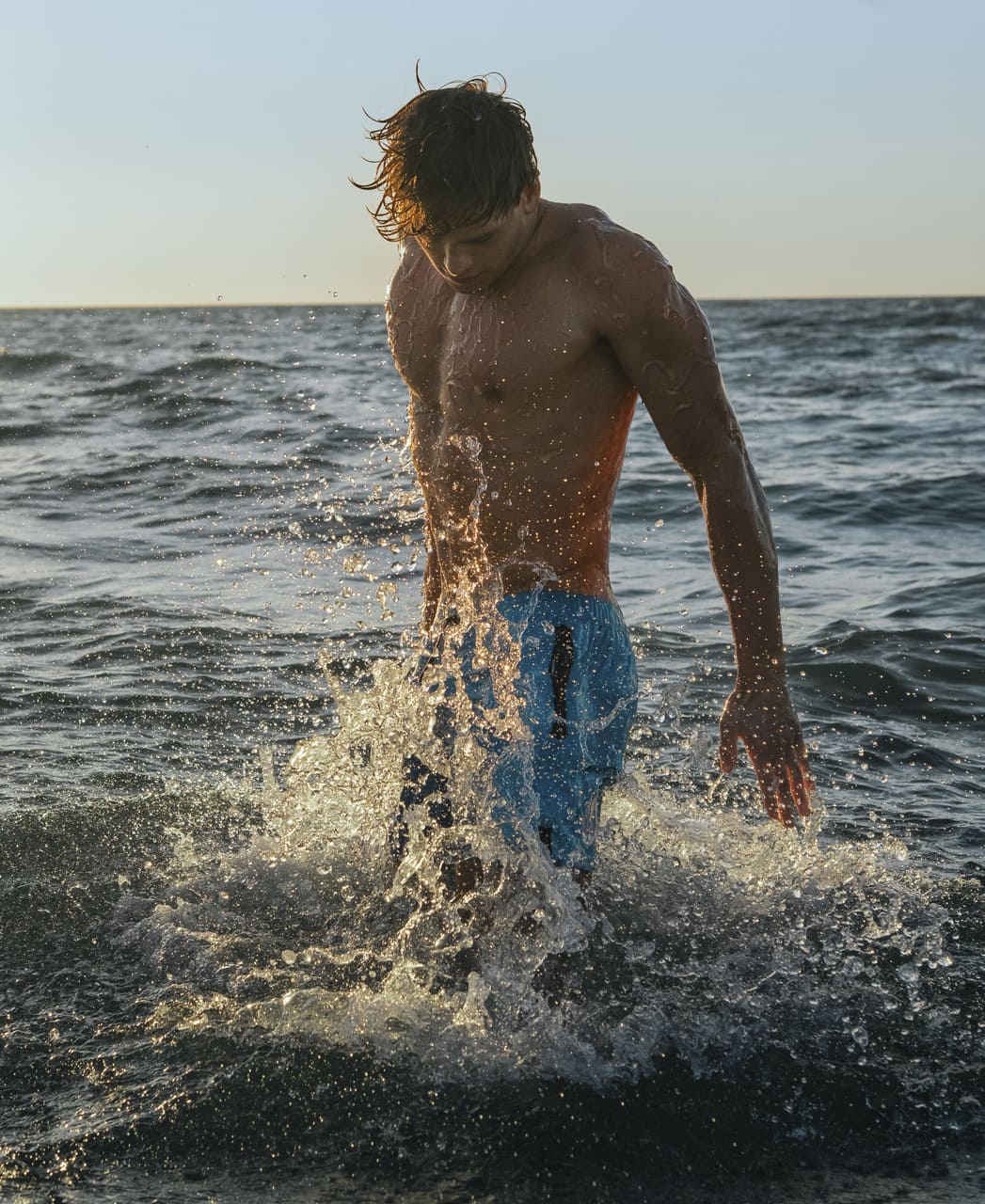Karlmaður gengur upp úr sjónum í túrkísbláum Arena Evo Side Zip Pockets Beach Boxer sundbuxum