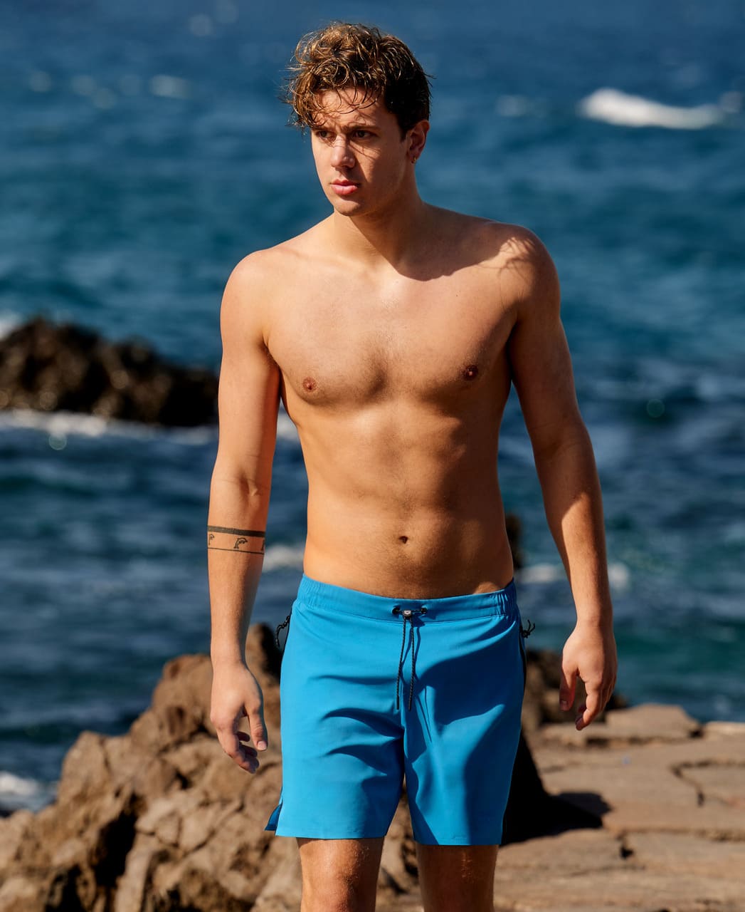 Karlmaður við sjóinn í túrkísbláum Arena Evo Side Zip Pockets Beach Boxer sundbuxum