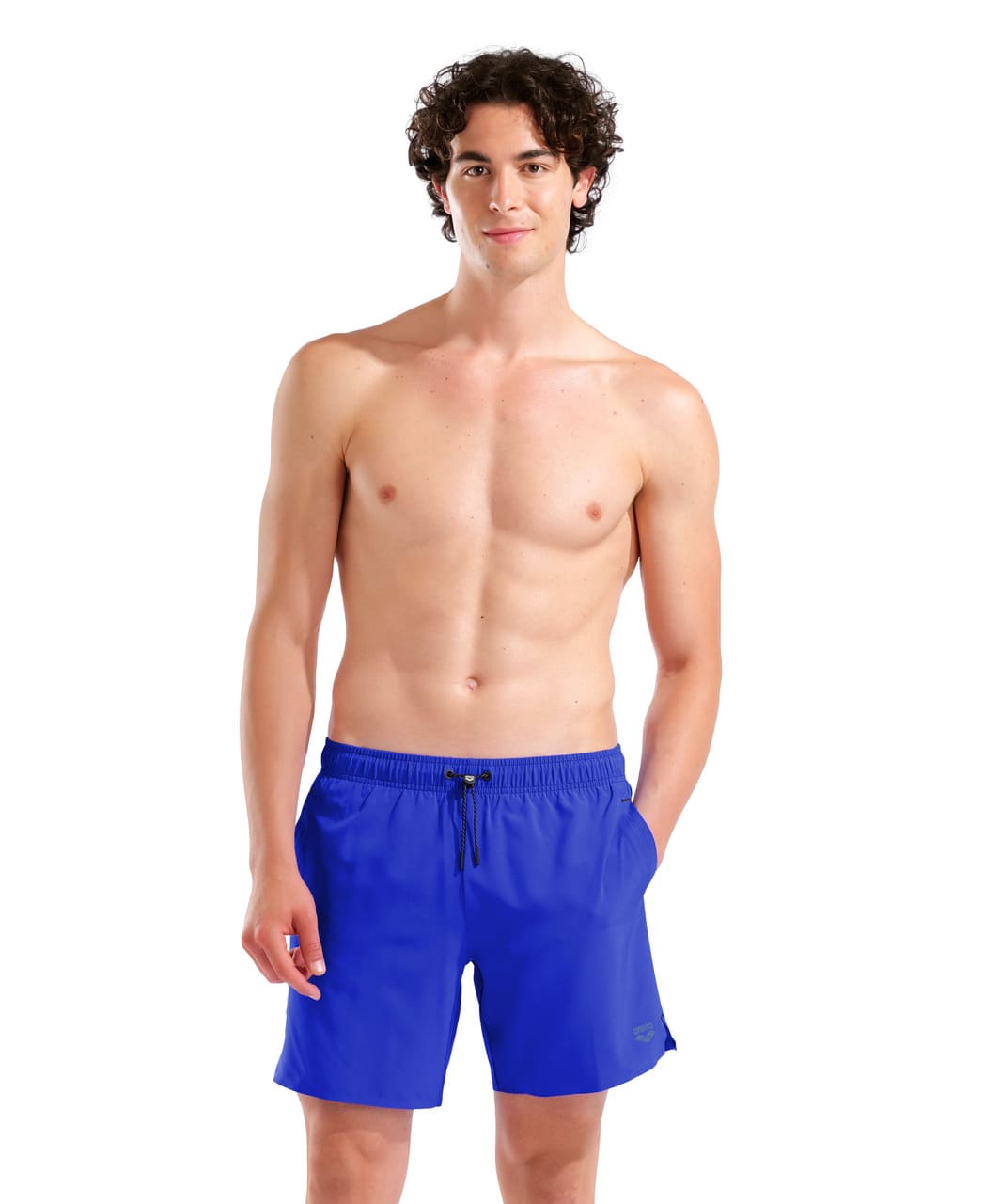 Brosandi karlmaður í neonbláum Arena Evo II Beach Boxer Solid sundbuxum með aðra hönd í opnum hliðarvasa, framhlið með reim og hliðarvösum sýnileg.