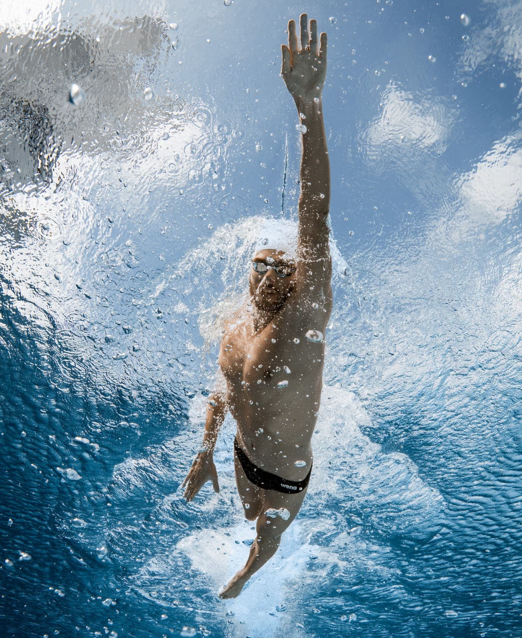 Sundmaður í svartri Arena Team Swim Brief Solid sundskýlu í straumlínulagaðri stöðu undir vatni, stutt snið sem dregur ekki úr hreyfanleika